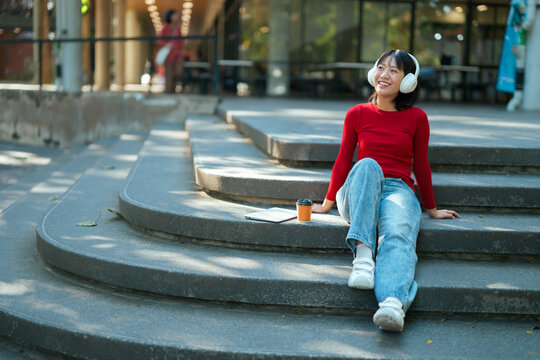 Student woman listening music on campus stairs enjoying coffee