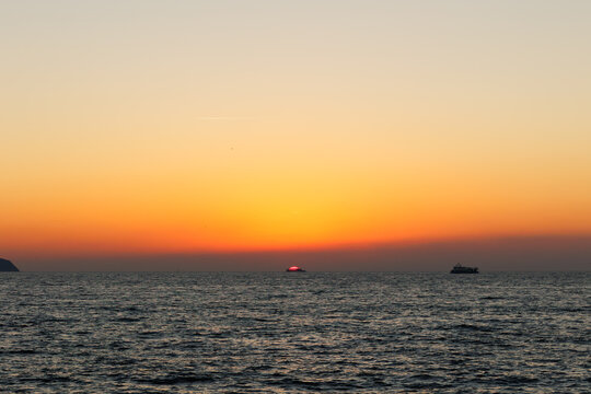 a ship going in front of the sun at a beautiful sunset over the sea with orange sky
