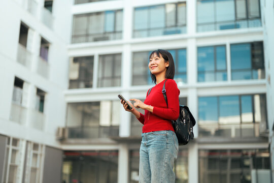 Young Asian woman smiling using smartphone outdoors