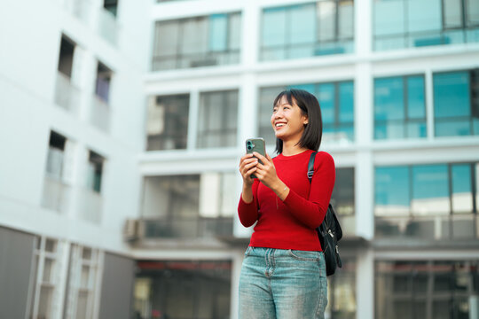 Happy young asian woman using smartphone outdoors