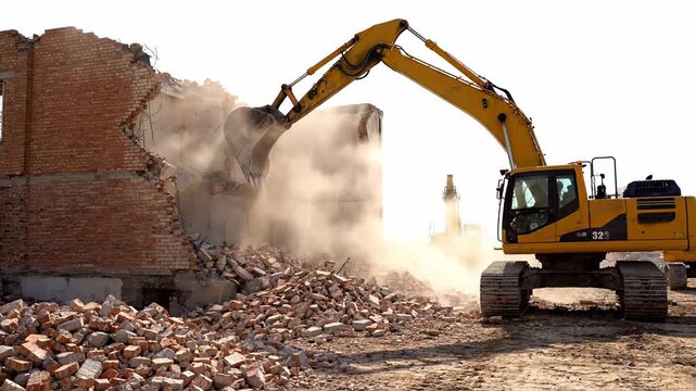 Industrial excavator equipped with a bucket is demolishing a decrepit brick building, causing rubble and billowing dust clouds to envelop the construction site against a white background