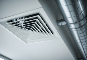 Obraz premium Modern HVAC ceiling air diffuser and metal ductwork installation | Low angle view of industrial ventilation system components | White ceiling supply grille and galvanized steel pipe 