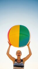 Young woman holding a vibrant colorful beach ball overhead smiling happily at summer vacation fun