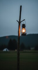 A glowing vintage oil lantern hangs from a rustic wooden pole illuminating the serene outdoor evening landscape