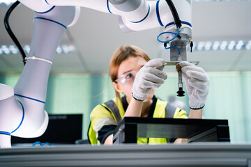 A woman in a yellow vest is working on a robot