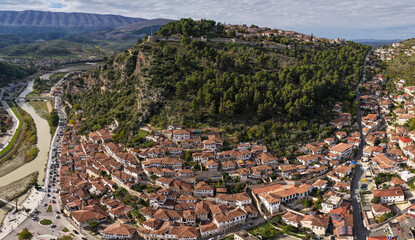 Aerial view of Berat Castle perched on a forested hill above the traditional white-roofed homes lining the Osum River.