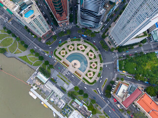 A city view with a large round plaza in the middle. The plaza is surrounded by buildings and has a fountain in the center. There are many cars and people walking around the plaza