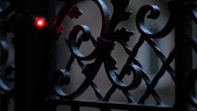 Iron fence with scrollwork detail, red light at night, dark aesthetic.