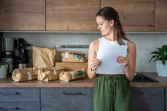 Young woman checking a list while looking at unpacked meal kit ingredients organized by recipe. Concept of planning weekly cooking using convenient pre-portioned grocery delivery.