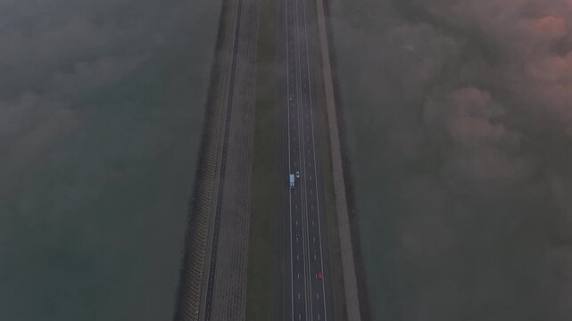 Afsluitdijk from above at sunrise, a road dividing low clouds and Dutch waters.