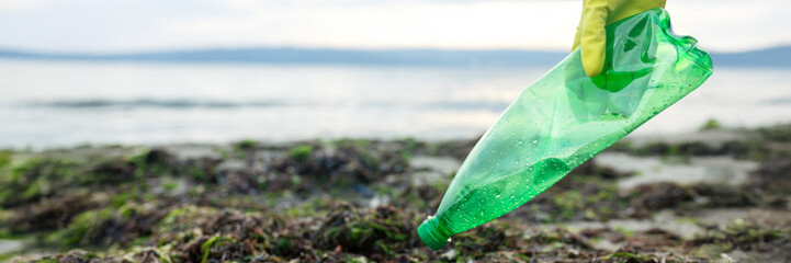 Volunteer picking up a green plastic bottle during beach cleanup, highlighting pollution, waste removal, and environmental protection.