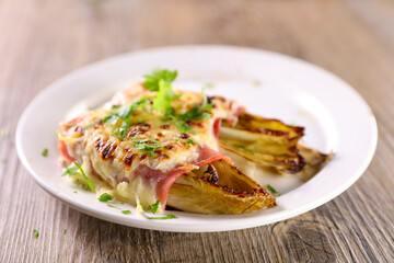 delicious baked chicory with ham and cheese on white plate