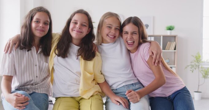 4 happy school children girls attend same class, become good friends, have fun during break time, pose for group photo together and look at camera with joyful smiling cheerful excited face expressions
