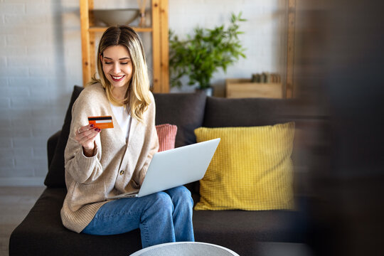 Smiling woman using credit card and laptop at home, representing fintech innovation, digital finance - Powered by Adobe