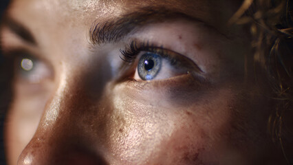 Naklejka premium Intense Gaze: Close-Up of a Blue Eye, Dramatic Lighting, Detailed Skin Texture.