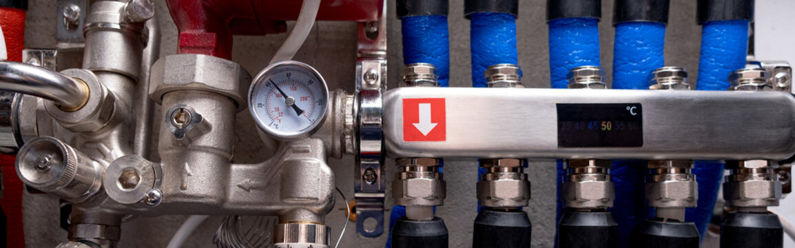 Complex residential heating manifold system with valves, gauges, and piping network. banner