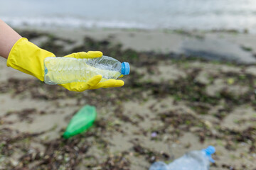volunteer collecting plastic bottles on a polluted beach, highlighting ocean pollution, waste problem, environmental protection and coastal cleanup action.