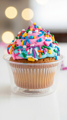 Festive cupcake in container with colorful sprinkles on top  