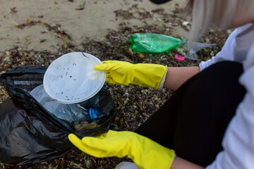 Volunteer collecting plastic waste and litter into a black trash bag during beach cleanup, highlighting pollution, environmental protection, sustainability, and eco awareness.