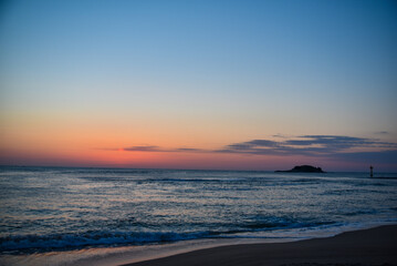 The ocean is calm and the sky is a beautiful shade of blue. The sun is setting and the sky is filled with a warm orange glow