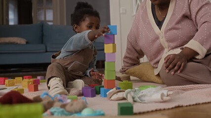Adorable Black toddler girl sitting on floor, building colorful toy block tower, when it falls, she shows result to her loving mother - Powered by Adobe