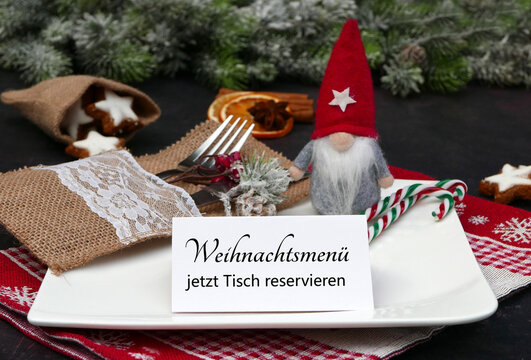 Weihnachtsmenü Tisch reservieren:  Gedeckter Tisch mit Tellern, Besteck, Weihnachtsdekoration und einer Karte mit der Aufschrift Weihnachtsfeier jetzt Tisch reservieren.