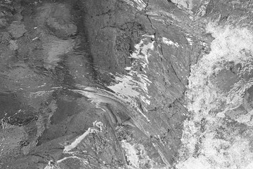 Monochrome view of rippling water flowing over textured rock in Mount Rainier National Park, highlighting natural patterns, reflections, and soft movement.