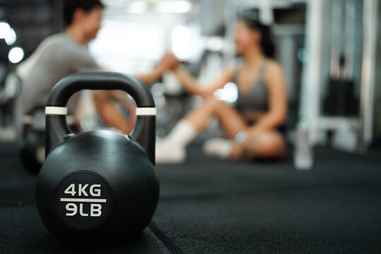 Asian woman and man sit in fitness gym with relax activity also look happiness after training and practice in fitness gym, focus kettlebell on floor - Powered by Adobe