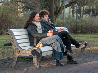 Man and woman sitting on a park bench and drinking coffee