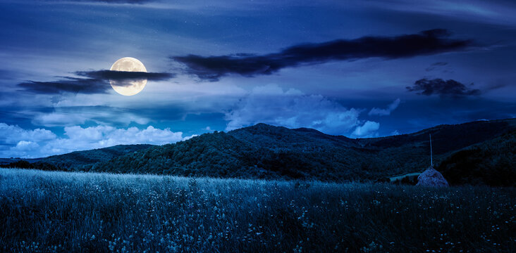 mountain landscape with haystack on the field at night. beautiful countryside scenery of Carpathians in summer under the sky with clouds in full moon light. finance investment or abstract concepts