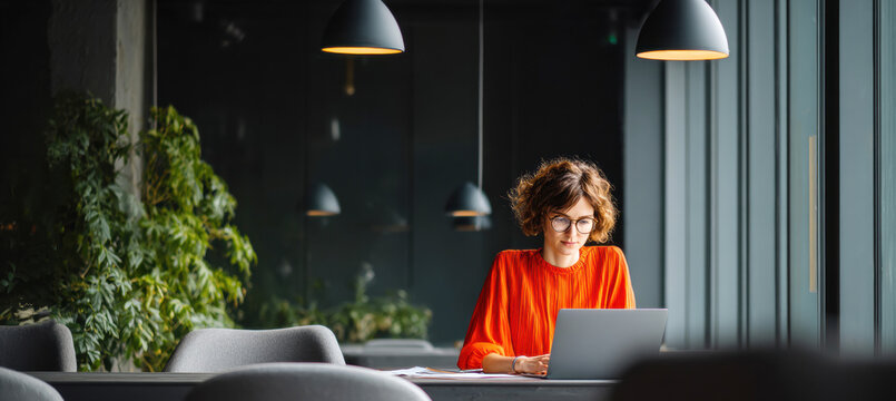Woman working on laptop in modern office space, focused on business tasks and remote project management