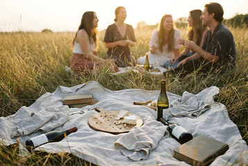 Friends Having a Sunset Picnic with Wine and Cheese in a Golden Field.