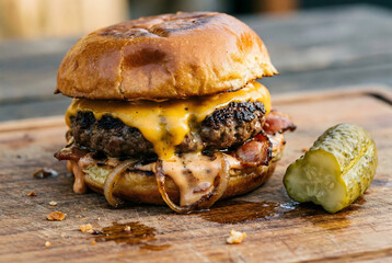 Close-up of Juicy Bacon Cheeseburger with Melted Cheddar and Spicy Sauce on a Wooden Board.