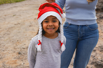 Happy indigenous female child smiling on camera while wearing santa claus hat and celebrating Christmas - Holiday, festive and childhood concept