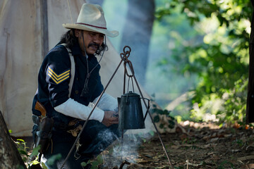 A cowboys sit at a rustic campsite, sharing a cup of coffee beside a wooden crate