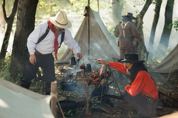 Group of cowboys preparing food at a campfire, roasting meat together in a warm