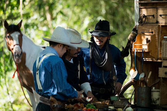 Cowboys gather around a chuck wagon preparing fresh ingredients for cooking