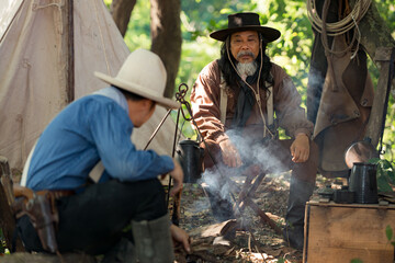 Two cowboys preparing food at a campfire, roasting meat together in a warm