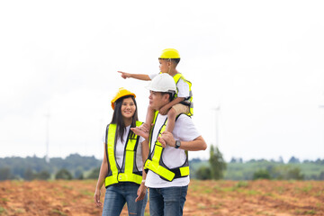 piggy back Asian Engineer family in field with wind turbines in background, Windmill. environmental renewable clean energy. Wind power generation. Solar panel. Windmill engineer inspection progress
