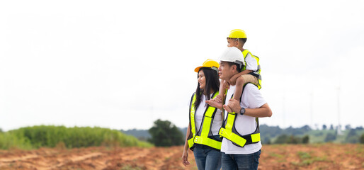piggy back Asian Engineer family in field with wind turbines in background, Windmill. environmental renewable clean energy. Wind power generation. Solar panel. Windmill engineer inspection progress