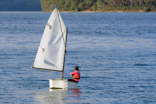 small sailboat is in the water with a young yachtsman in a red life jacket