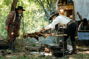 Two senior cowboys preparing food at a campfire, roasting meat together in a warm
