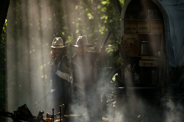 Two cowboys aiming rifles in a forest camp, with sunlight streaming through the smoke