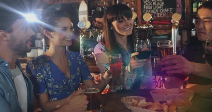 Four patrons raising glasses at bar table, woman lifting wine glass initiating animated clink rings