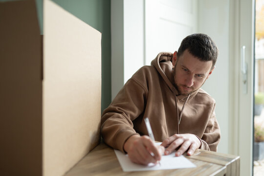 A man carefully prepares a parcel for postal shipment, demonstrating organized shipping procedures and streamlined return systems. Represents reliable logistics and efficient e-commerce operations. - Powered by Adobe