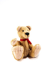 A hand made beige teddy bear wearing a red ribbon around its neck, isolated on a white background