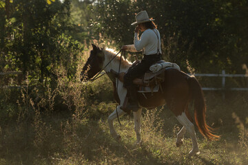 A cowboy riding a rearing horse in a fenced area surrounded by lush greenery