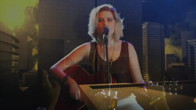 Woman singer playing guitar, singing for crowd on stage, lighting shifting cityscape overlaying her