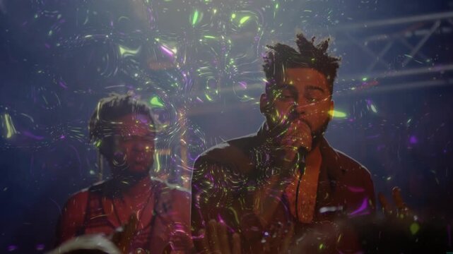 Male singer singing into mic in concert sparking lights painting bubbles on band, engaging fans