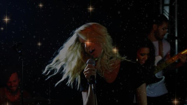 Lead vocalist performing on dim stage, band playing and music building sparkles accenting hair whip